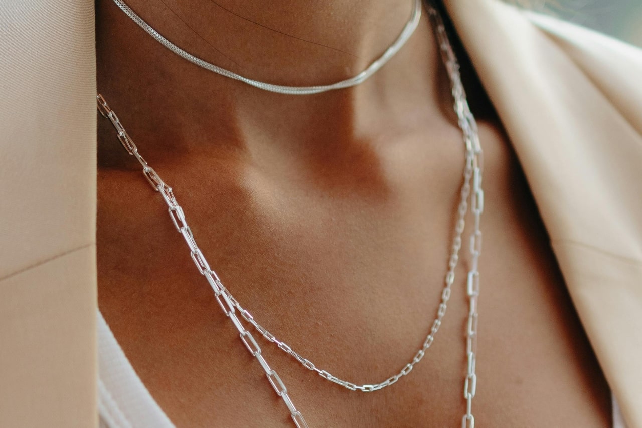 A close-up image of a woman&rsquo;s neckline adorned with three silver layered necklaces