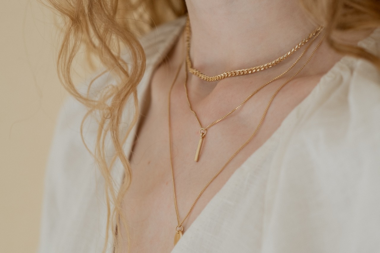 A close-up image of a woman&rsquo;s neckline adorned with three layered gold necklaces