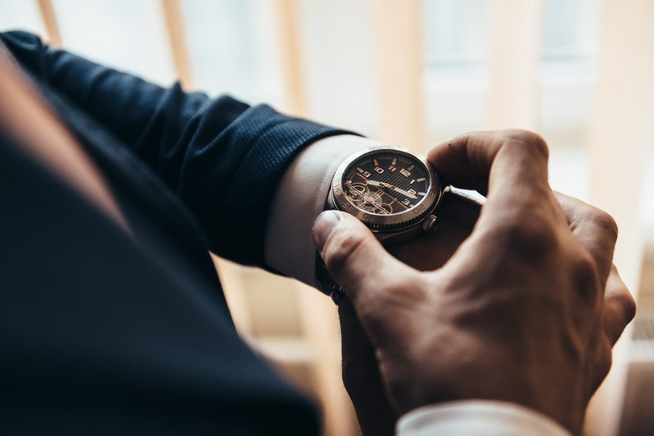 An over-the-shoulder view of a well-dressed man checking the time on his distinctive luxury watch.