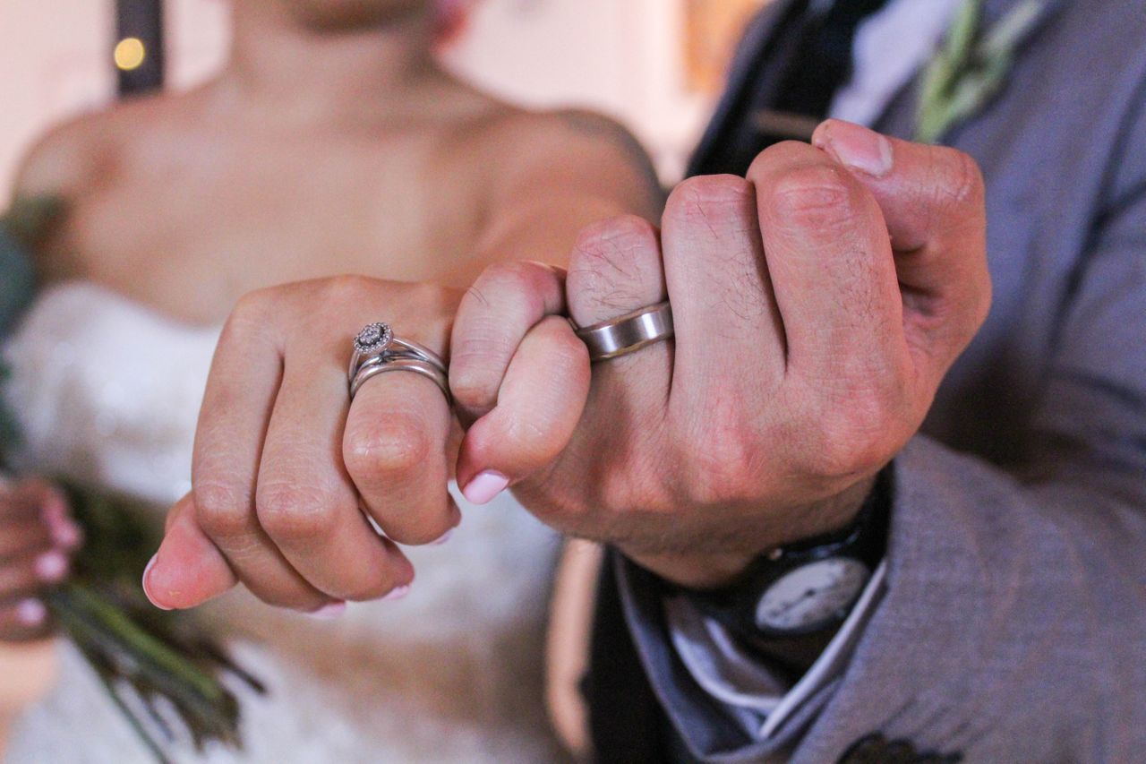 a man and a woman’s hands with their pinkies interlocked wearing wedding bands